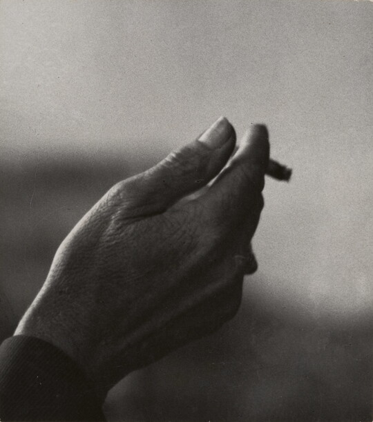 A black-and-white close-up photograph of a right hand holding an almost-finished cigarette.