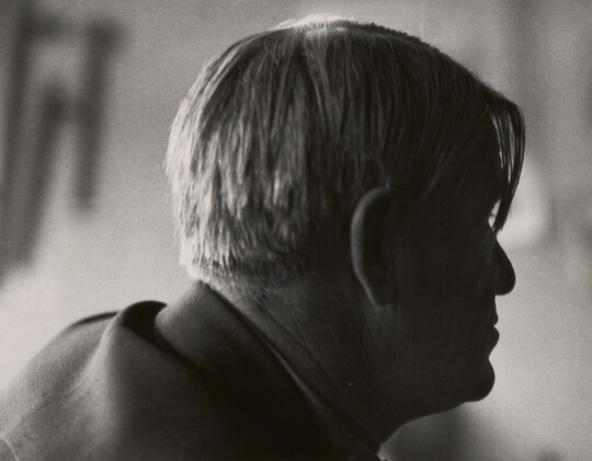 A black-and-white photograph of a man's head in profile with longer pieces of hair hanging over his right eye.