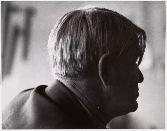 A black-and-white photograph of a man's head in profile with longer pieces of hair hanging over his right eye.