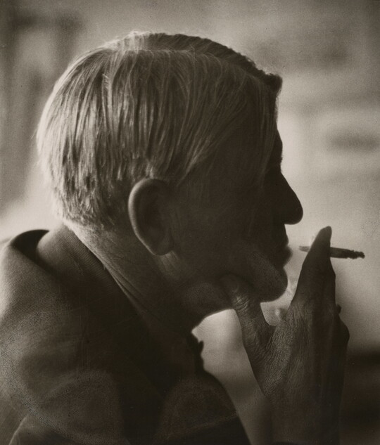 A sepia-toned photograph of a man's head in profile holding a cigarette posed in front of his lips.
