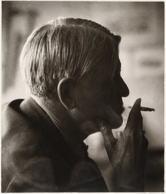 A sepia-toned photograph of a man's head in profile holding a cigarette posed in front of his lips.