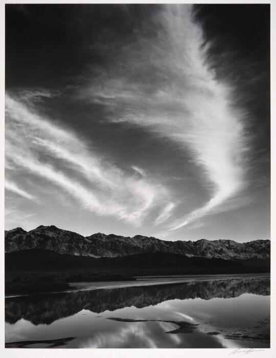 A black-and-white landscape photograph of mountains and clouds that reflect on the still water in the foreground.