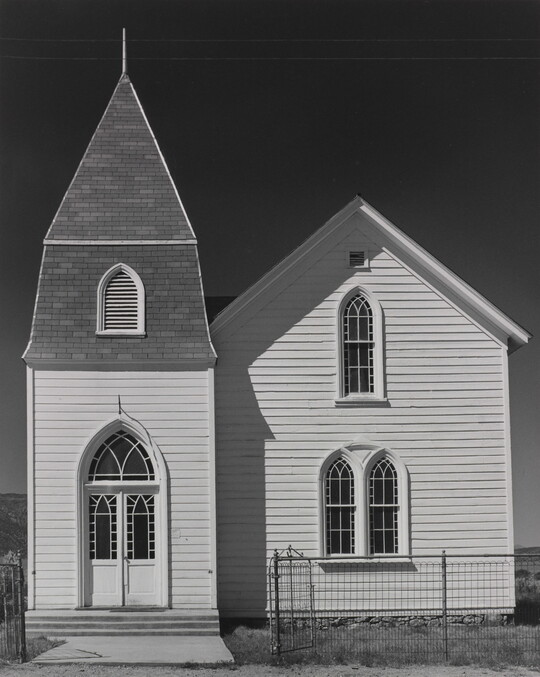A black-and-white photograph of a two-story church with white clapboard siding and arched windows and doors.