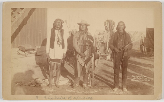 A sepia-toned photograph of three Indigenous men standing outside next to each other.