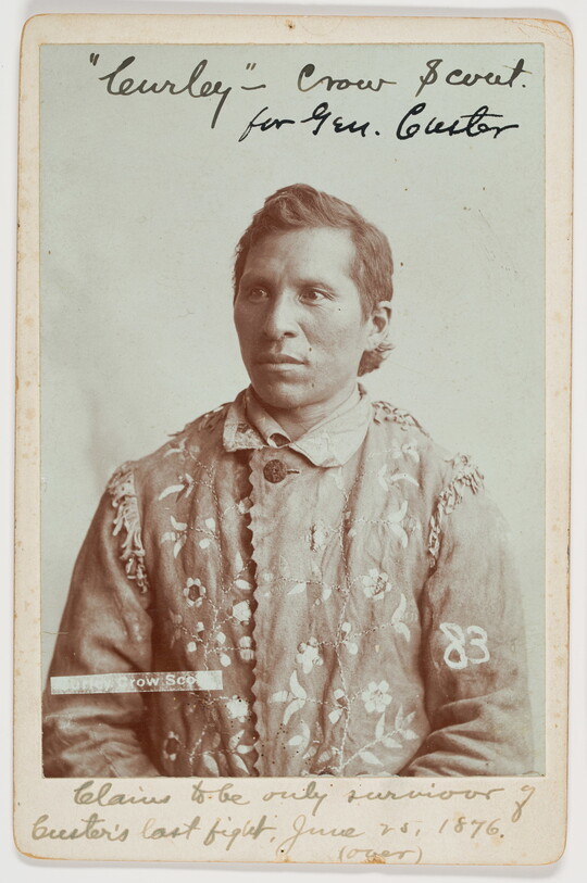 A sepia-toned portrait of an Indigenous man wearing a hide jacket with decorative stitching.