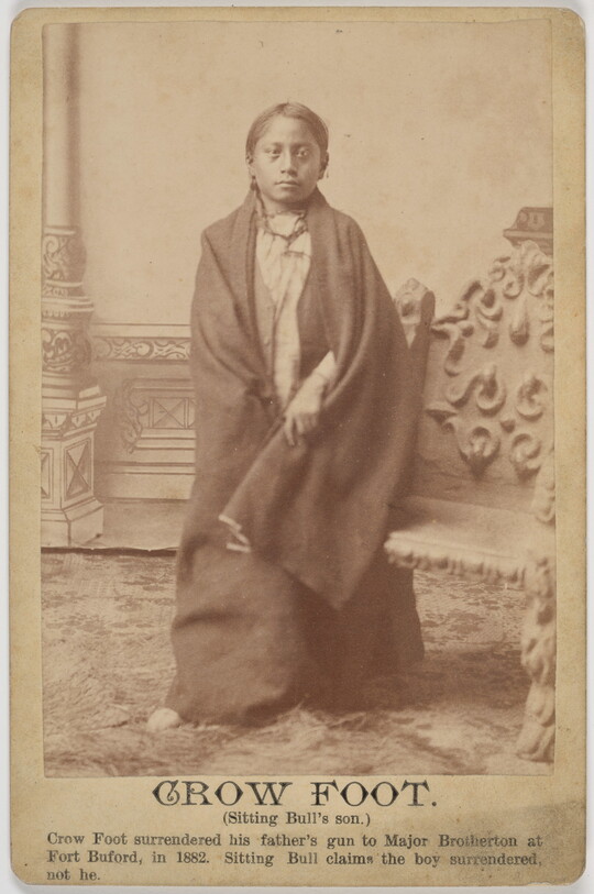 A sepia-toned portrait photograph of an Indigenous boy wrapped in a blanket.