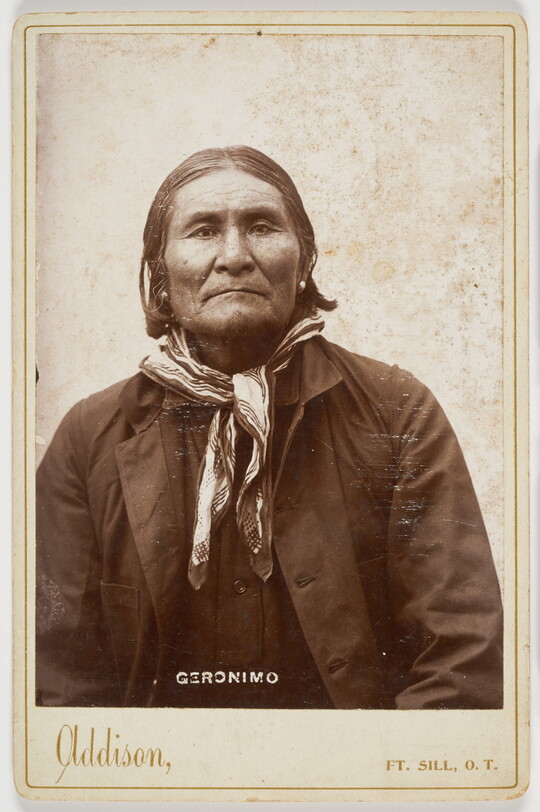A black-and-white formal portrait photograph of an Indigenous man in a shirt, jacket, and neckerchief.