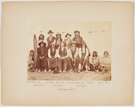 A sepia-toned photograph of a group of Indigenous people, some standing and some sitting.
