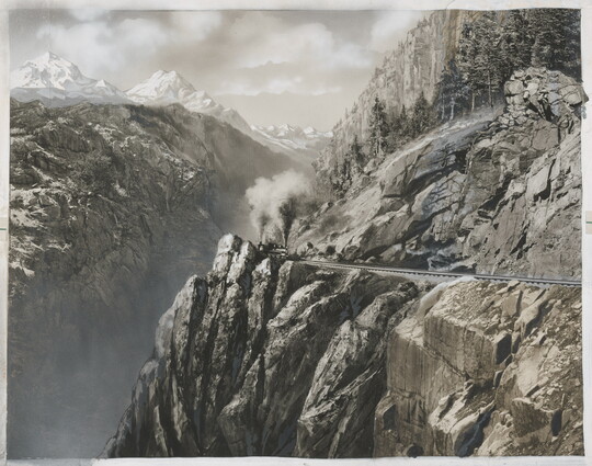 A black-and-white photograph with some hand-coloring of a train traveling along a steep ledge of a high mountain.