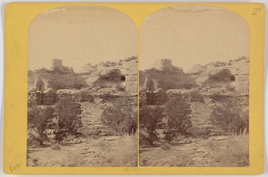 Two almost identical side-by-side sepia-toned photographs of cave dwellings in a high cliff with scrubby vegetation in the foreground.