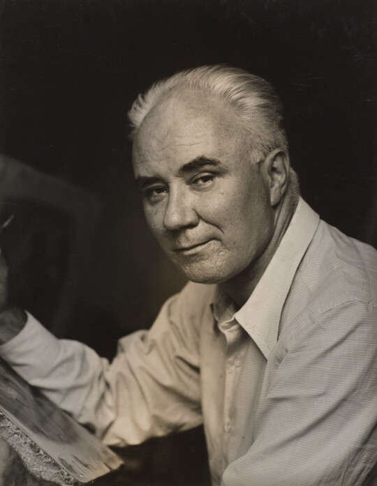 A black-and-white photograph of a middle-aged White man in three-quarter view leaning on something in front of him with his forearm.