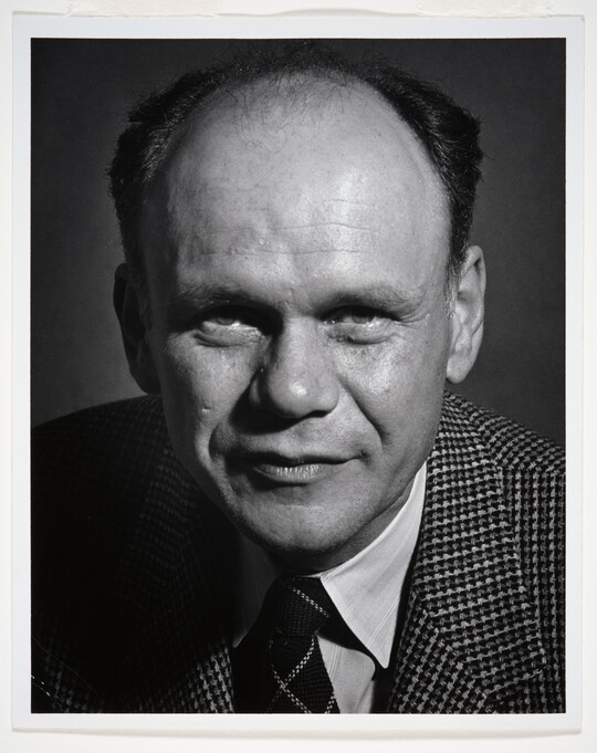 A black-and-white portrait photograph of a balding White man wearing a houndstooth blazer and striped tie.