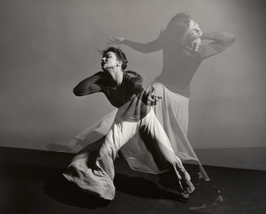 A double-exposed, black-and-white photograph of a female figure dancing dramatically.