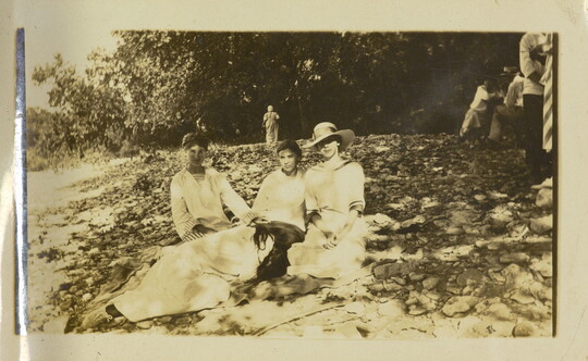 A sepia-toned photograph of four White women, three sitting and one lying with her head on the lap of another, on a rocky slope.