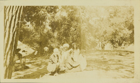 A faded sepia-toned photograph of six White women crouched next to a tent at a campsite.