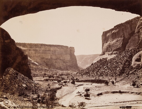 A sepia-toned photograph of tall cliffs on either side of a dry gully, framed by the bottom of an arch.