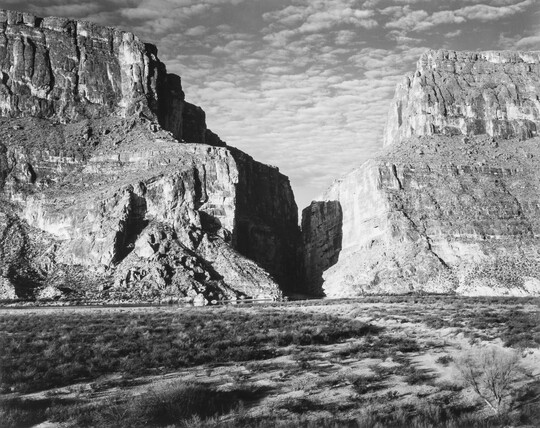 A black-and-white photograph of a canyon between two large mountains.