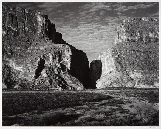 A black-and-white photograph of a canyon between two large mountains.