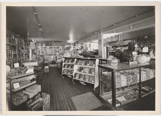 A black-and-white photograph of the interior of a grocery store from the early 20th century.