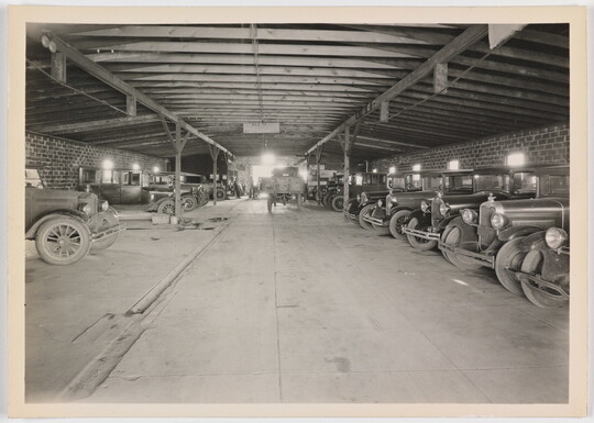 A black-and-white photograph of early models of cars in a covered garage.