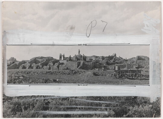 A black-and-white photograph of people standing on an excavation site; crop marks and white paint mark how the photo should be cropped.