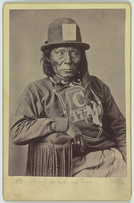 A black-and-white portrait photograph of a seated Indigenous man wearing a long-sleeved t-shirt and bowler hat.