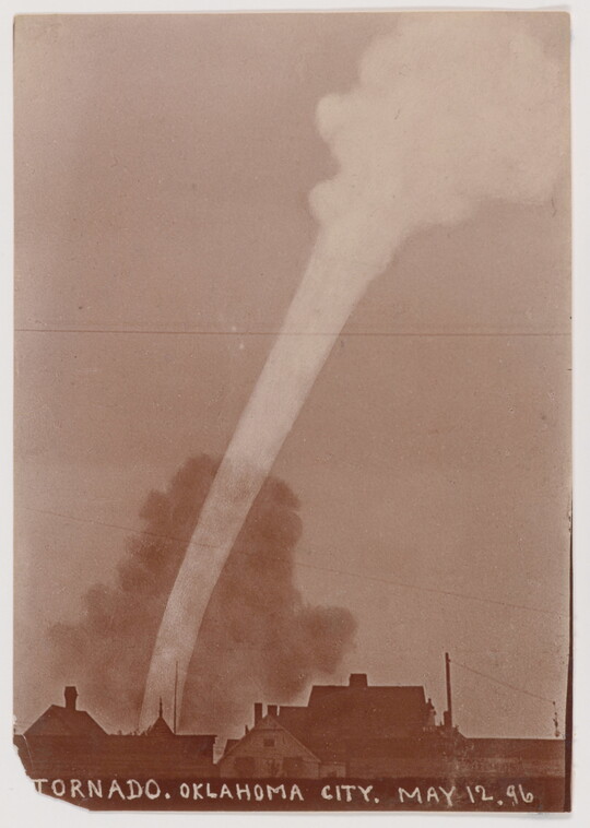 A sepia-toned photograph of a white funnel cloud above the silhouette of a town.