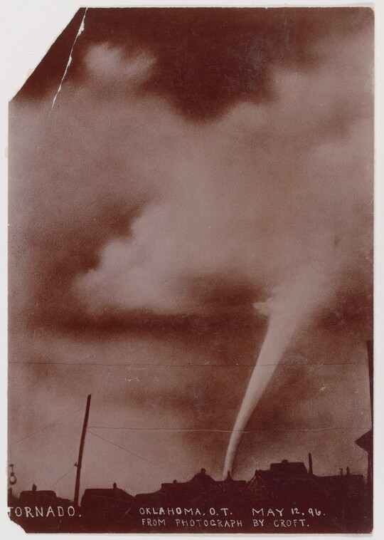 A sepia-toned photograph of a white funnel cloud above the silhouette of a town.