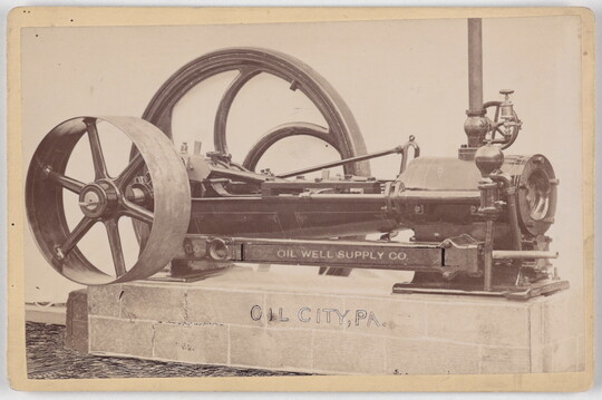 A black-and-white photograph of a machine with two wheels of varying sizes sitting on a concrete base.