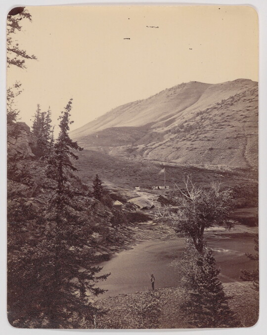 A black-and-white photograph of an aerial view of a mountain lake and a person fishing on the shore.