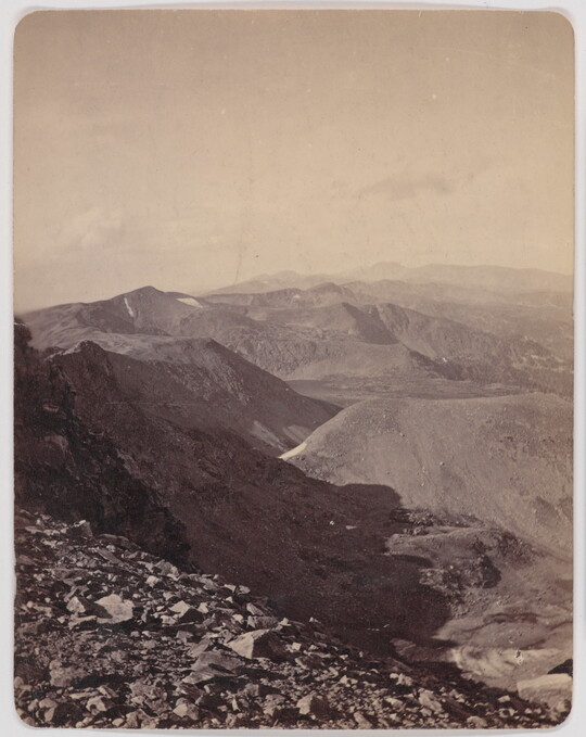 A black-and-white photograph of rocky mountains under a clear sky viewed from a high elevation.