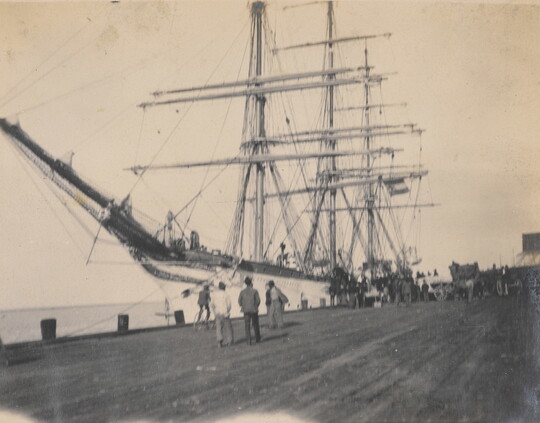 A black-and-white photograph of people on a dock looking at a large ship.