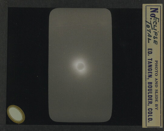 A black-and-white slide of the sun completely eclipsed by the moon against a dark sky.