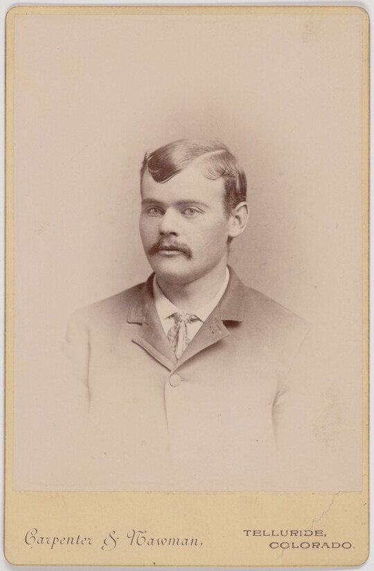A black-and-white portrait photograph of a White man with a mustache wearing a jacket and tie.