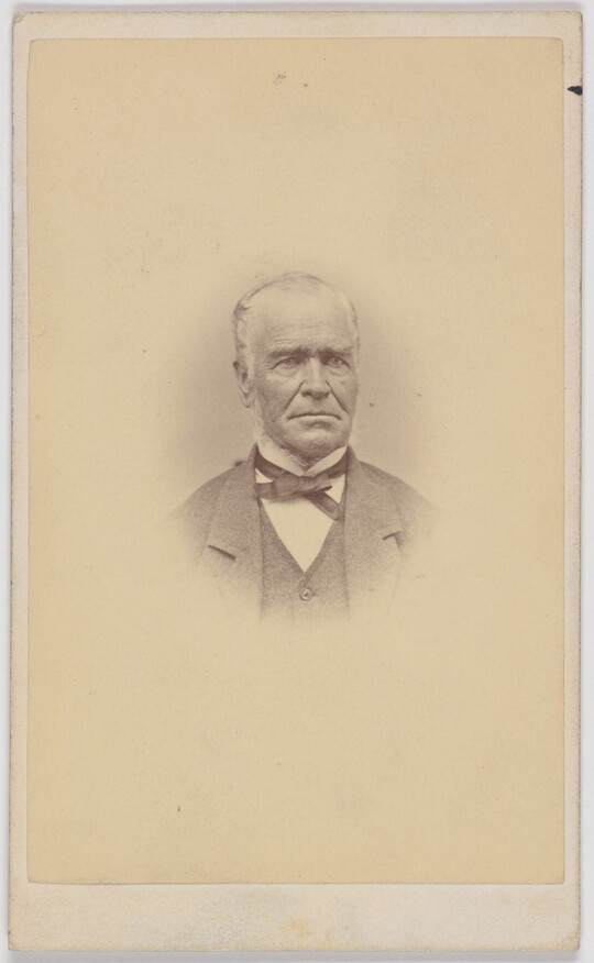 A black-and-white portrait photograph of an older White man, balding, wearing a bow tie, jacket, and vest.