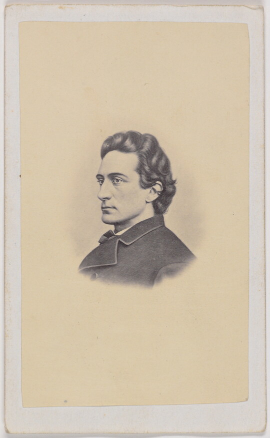 A black-and-white portrait photograph of a young White man in profile with dark wavy hair, wearing a dark overcoat.