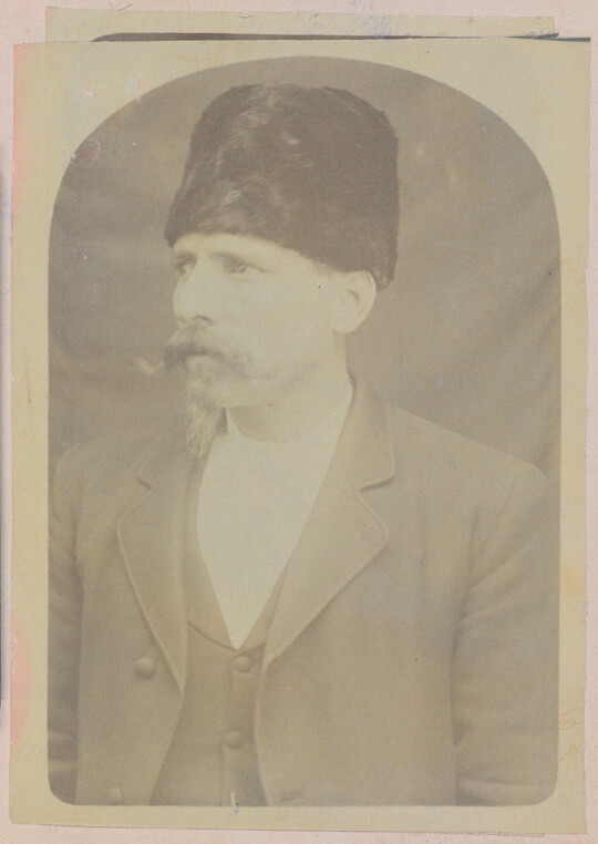 A faded sepia-toned portrait of a White man with a handlebar moustache wearing a fur Cossack-stye hat and a three-piece suit.