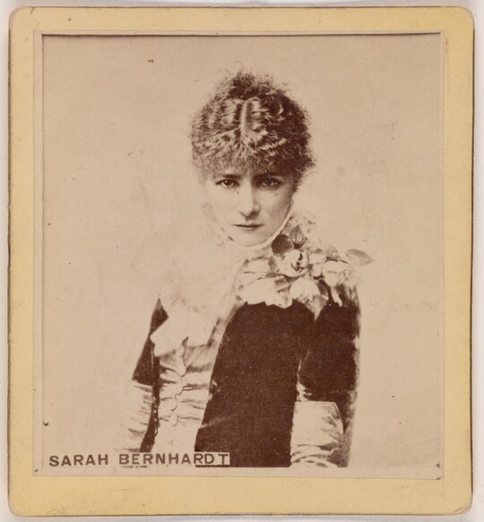 A sepia-toned portrait photograph of a young, White woman from the waist up, wearing formal, early 20th century clothing.