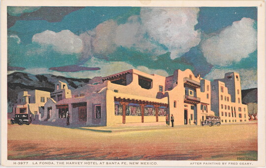 A color postcard of an adobe building with mountains and fluffy white clouds in the background.