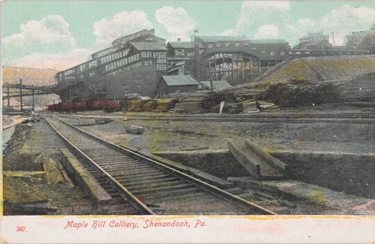 A color postcard of railroad tracks beside an industrial building.