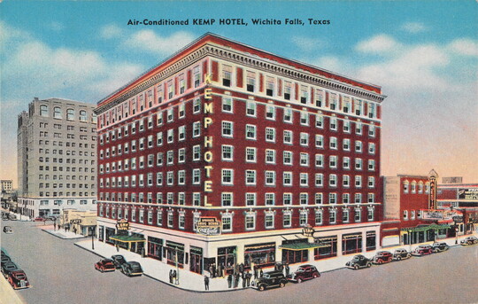 A color postcard of a multi-story red brick hotel building on a street corner.
