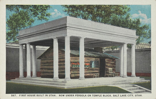 A color postcard of a log cabin covered by a columned structure.