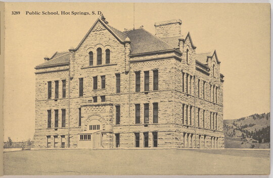 A sepia-toned photograph of a four-story stone building on a grassy lawn with the label "Public School, Hot Springs. S.D."