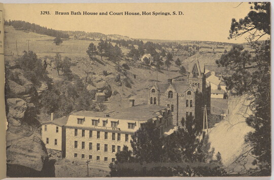 A sepia-toned photograph of large stone buildings in a valley with "Braun Bath House and Court House, Hot Springs, S.D." printed across the top.