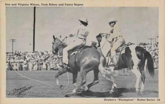 A black-and-white postcard of a cowgirl and cowboy on horseback performing at an outdoor rodeo.