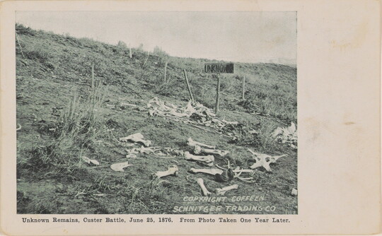 A black-and-white photograph of a field with human bones scattered everywhere and a wooden sign that reads, "UNKNOWN."