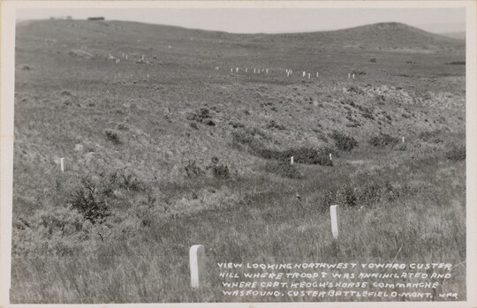 A black-and-white photograph postcard of grassy hills and scattered grave markers.