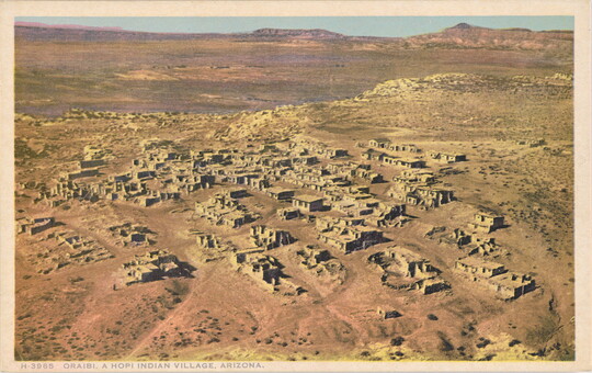A color postcard of a bird's eye view of a small village in a dusty orange desert landscape.
