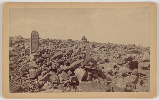A sepia-toned photograph of two gravestones surrounded by large rocks.