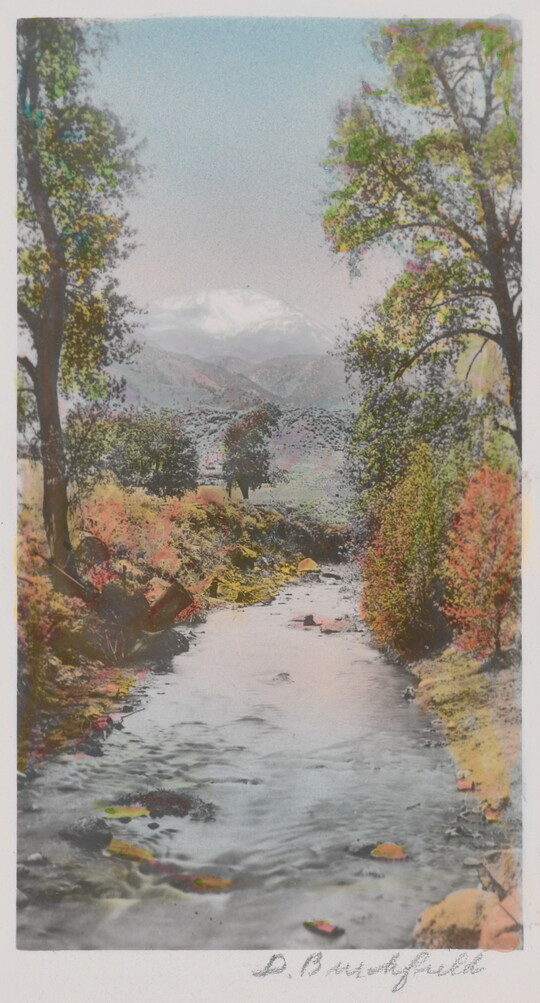 A color photograph of a river disappearing into the distance, trees in autumn colors on the banks, and snowy mountains in the distance.
